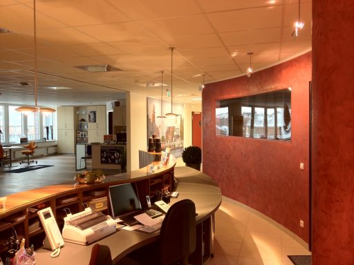 Helle Empfangszone mit runder Theke und rot gestrichener Wand, Büros im Hintergrund.