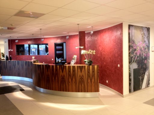Empfangsbereich mit Holztheke und rot gerippter Wand, neben einem Blumenmotiv.