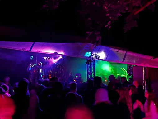 Farbenfrohe Lichtshow und Menschenmenge bei einer nächtlichen Party im Freien.